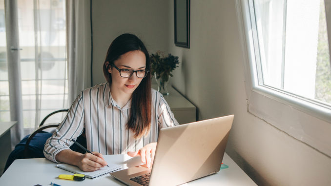 Hübsche Studentin mit Brille sitzt am Laptop.