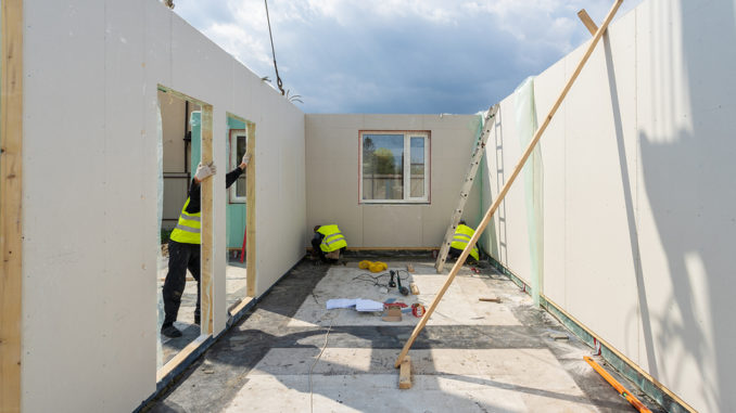 Bauprozess neues und modernes modulares Haus aus Verbundschluckplatten. Drei Baumeister in einheitlicher Abnutzung, die an der Gebäudeentwicklungsindustrie des energieeffizienten Eigentums arbeiten