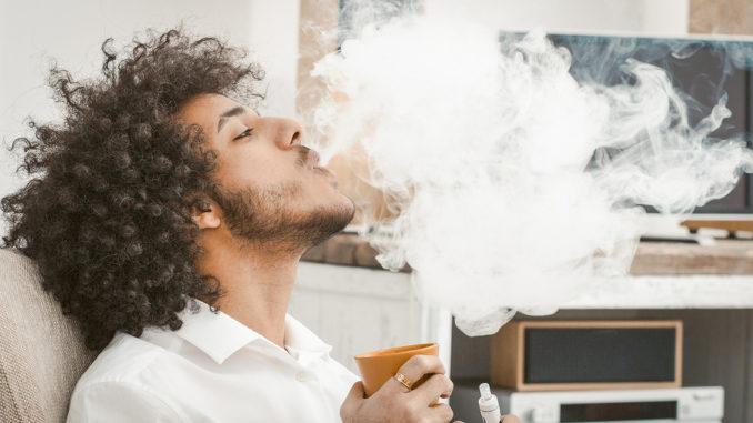 Ein junger Mann mit Afro raucht in der eigenen Wohnung